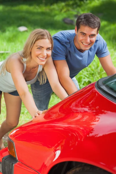 Smiling couple pushing their broken down car — Stock Photo, Image