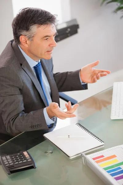 Un hombre de negocios sentado en su escritorio explicando algo — Foto de Stock
