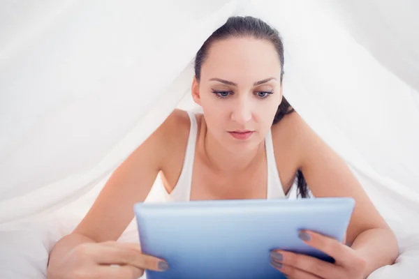 Gelukkig brunette liggen onder de lakens met behulp van haar tablet-pc — Stockfoto