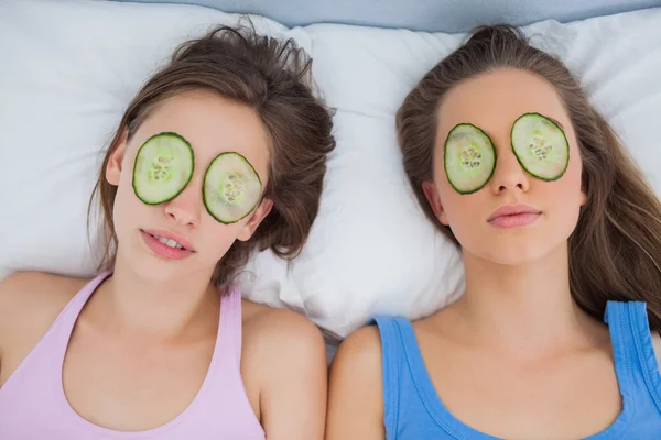 Friends lying in bed with cucumber slices on eyes — Stock Photo, Image