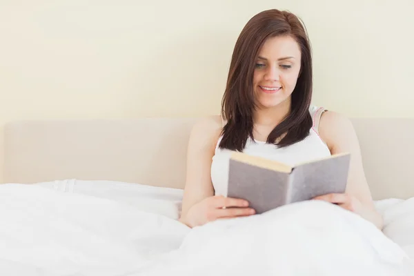 Chica sonriente leyendo un libro acostado en una cama — Foto de Stock