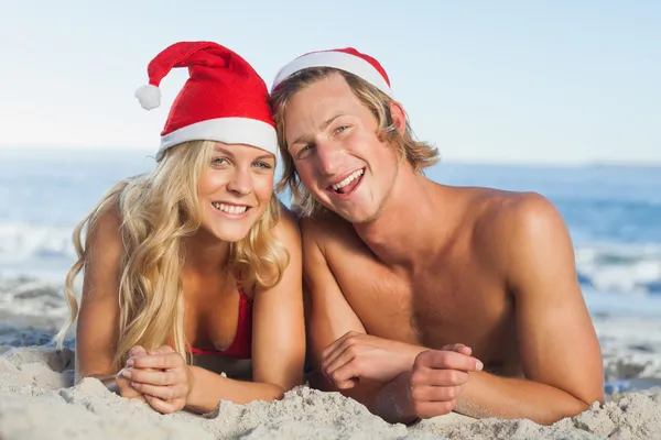 Coppia sdraiata sulla spiaggia indossando cappelli di Natale — Foto Stock