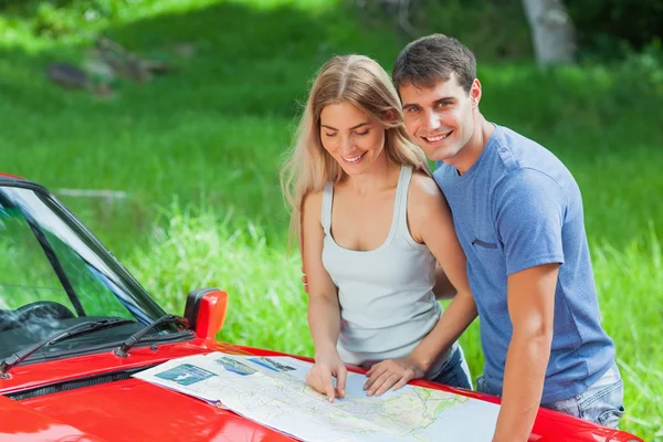 Cheerful young couple reading map on their cabriolet bonnet — Stock Photo, Image