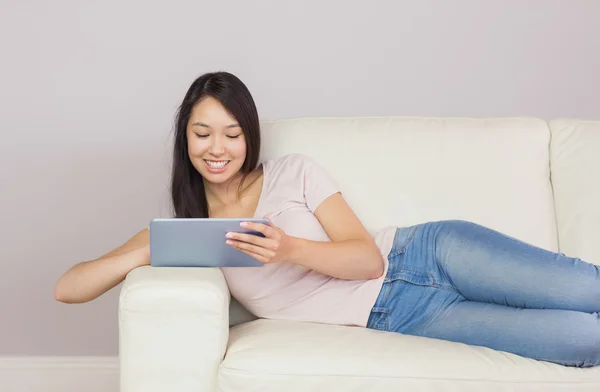 Красивая азиатка лежит на диване с помощью цифрового планшета — стоковое фото