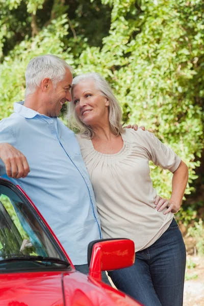 Smiling mature couple leaning against their red cabriolet — Stock Photo, Image