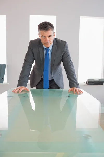 Serious businessman standing in front of a desk — Stock Photo, Image