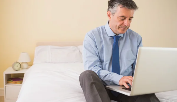 Uomo concentrato utilizzando un computer portatile seduto su un letto — Foto Stock