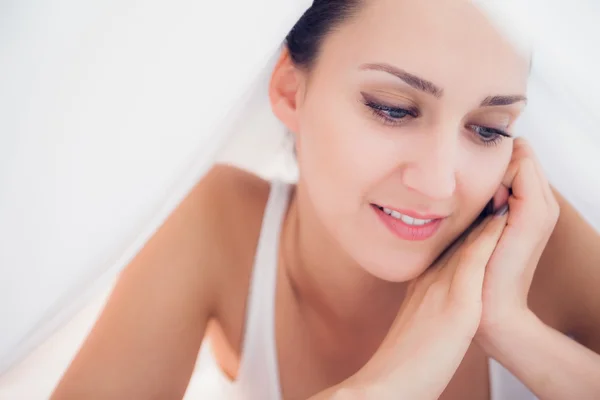 Gelukkig brunette liggen onder de lakens neer te kijken — Stockfoto