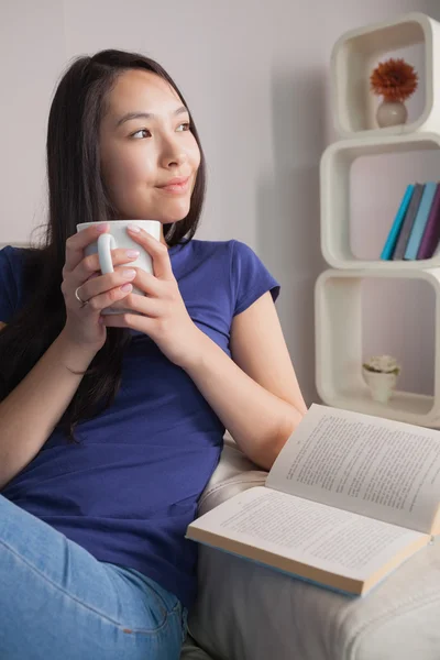 Pensando mujer asiática sentada en el sofá sosteniendo taza de café —  Fotos de Stock