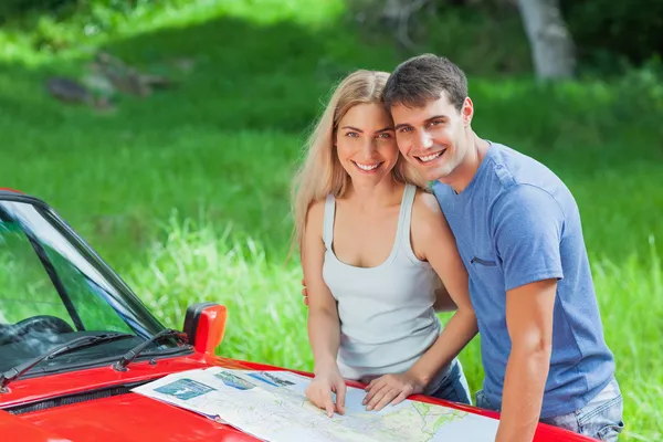 Felice giovane coppia lettura mappa sul loro cofano cabriolet — Foto Stock