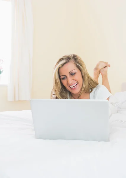Eğlenerek kadın yatağında yatan bir dizüstü bilgisayar kullanarak — Stok fotoğraf