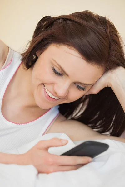 Fröhliches Mädchen mit einem Handy, das auf einem Bett liegt — Stockfoto