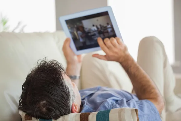 铺设在使用 tablet pc 的沙发上的男人 — 图库照片