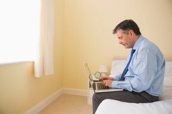 Uomo concentrato utilizzando un computer portatile seduto su un letto — Foto Stock