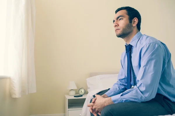 Thinking man looking away sitting on his bed — Stock Photo, Image