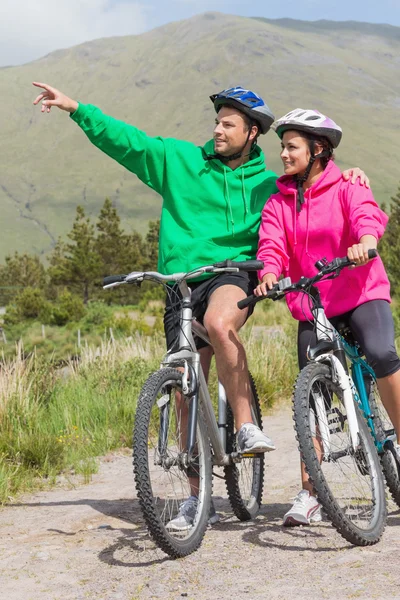 Athletic couple on a bike ride wearing hooded jumpers with man pointing — Stock Photo, Image