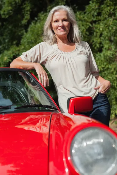 Улыбающаяся зрелая женщина, прислонившаяся к своей красной кабриолете — стоковое фото