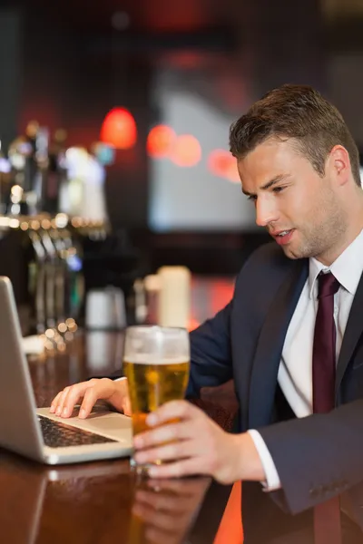 Zakenman met een drankje terwijl u werkt op zijn laptop — Stockfoto