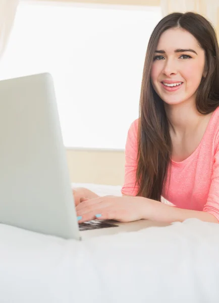 Young girl looking at camera using a laptop lying on a bed — Stock Photo, Image