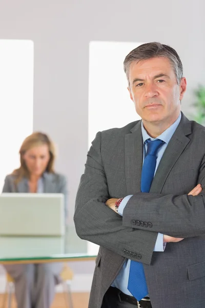 Irritato uomo d'affari guardando fotocamera braccia incrociate con una donna d'affari che lavora su sfondo — Foto Stock