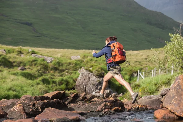 Athletic hiker leaping across rocks in a river — Stock Photo, Image