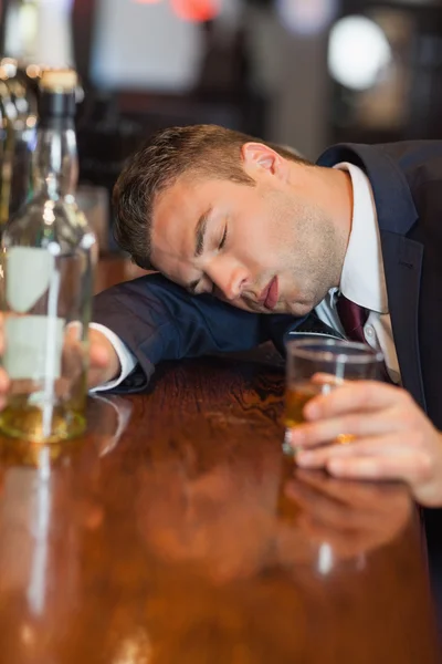 Drunk businessman holding whiskey glass lying on a counter — Stock Photo, Image