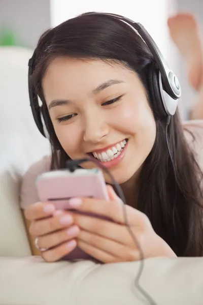 Alegre ásia menina deitado no o sofá e ouvir a música com smartphone — Fotografia de Stock