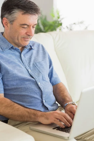 Koncentrovaná muže, který seděl na pohovce, psaní na notebooku — Stock fotografie