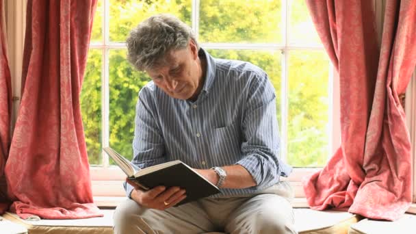 Focalisé homme mûr assis près d'une fenêtre la lecture d'un livre — Video