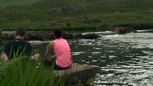 Par avkopplande vid en lugn sjö på landsbygden — Stockvideo