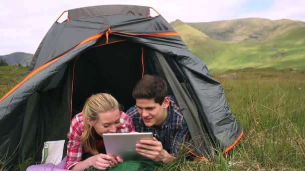 Happy couple using a digital tablet lying in their tent — Stock Video