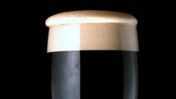 Foam head settling on pint of stout on black background — Stock Video