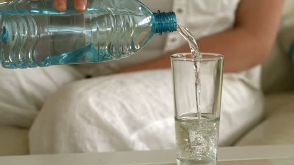 Mladá žena sedící na gauči, nalil sklenici vody — Stock video