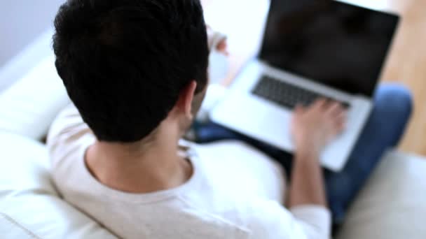 Mann trinkt einen weißen Kaffee, während er seinen Laptop benutzt — Stockvideo