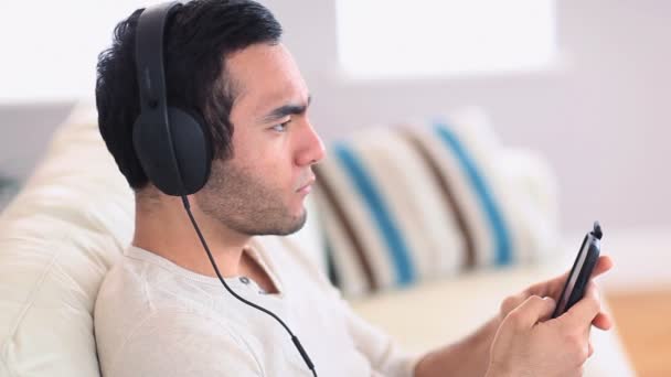 Hombre guapo con auriculares escuchando música en su teléfono inteligente — Vídeos de Stock