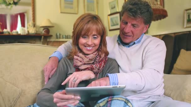 Pasangan dewasa yang duduk di sofa menggunakan tablet pc mereka — Stok Video