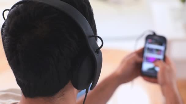 Schöner Mann mit Kopfhörern, der Musik auf seinem Smartphone auswählt — Stockvideo