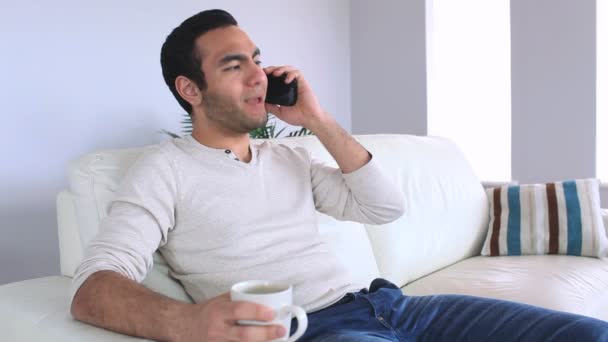 Όμορφος άντρας, απαντώντας στο τηλέφωνο ενώ χαλαρώνετε στον καναπέ του — Αρχείο Βίντεο