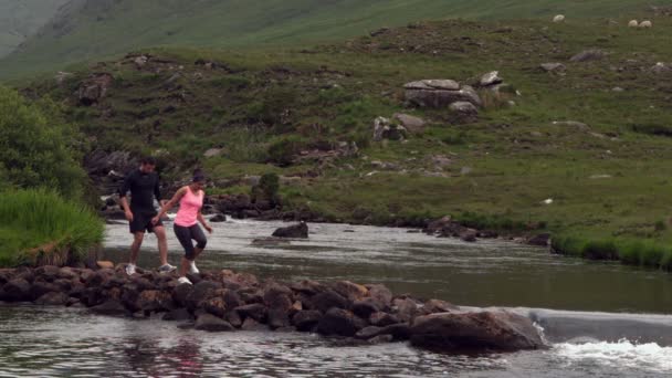Paar überquert Felsen inmitten eines fließenden Flusses — Stockvideo