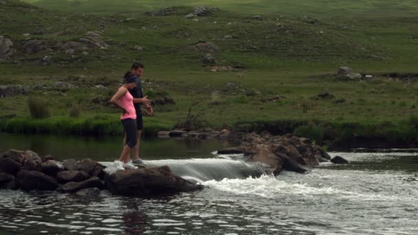 Pareja de pie sobre rocas en medio de un río — Vídeos de Stock