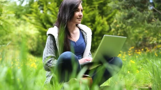 Vrouw zitten op gras met behulp van haar laptop — Stockvideo