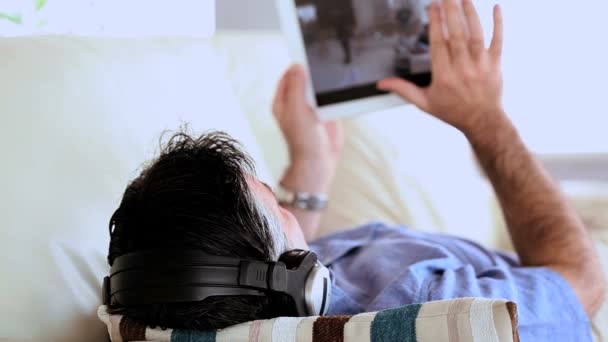 Zralý muž leží na gauči, poslouchá hudbu a použití počítače tablet pc — Stock video