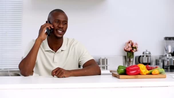 Мужчина на кухне разговаривает по телефону — стоковое видео