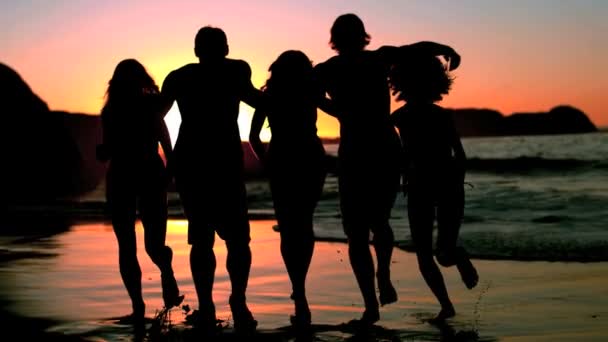 Amigos corriendo hacia el mar bajo el atardecer — Vídeo de stock