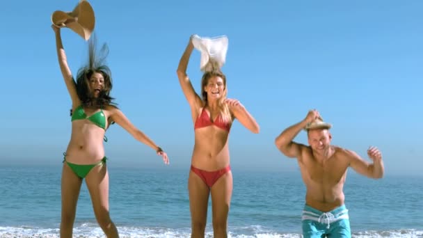 Attractive friends jumping on the beach while raising their hat — Stock Video