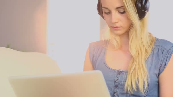 Mooie tiener met behulp van laptop op haar bank en luisteren naar muziek — Stockvideo