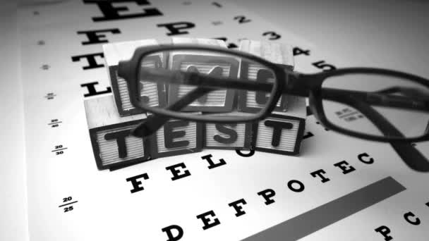 Glasses falling next to blocks spelling out eye test in black and white — Stock Video