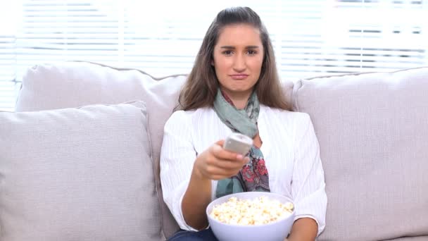 Брюнетка смотрит телевизор и ест попкорн — стоковое видео