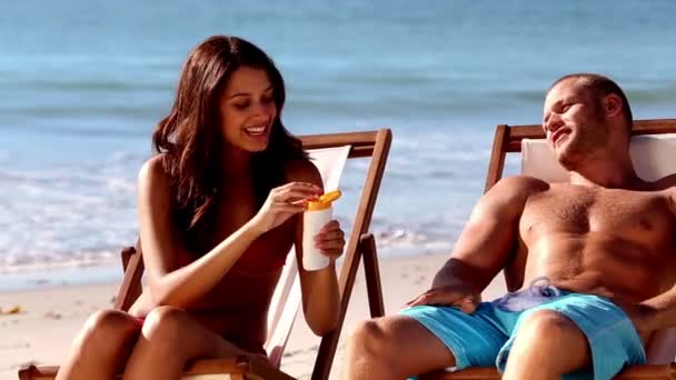 Веселая женщина наносит солнцезащитный крем своему парню — стоковое видео