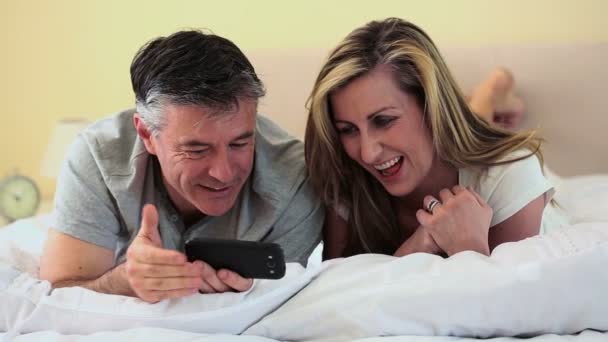 Зрелая пара лежит на кровати и смотрит на смартфон — стоковое видео
